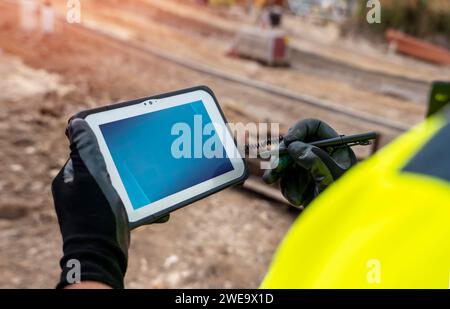 Site engineer surveyor using rugged tablet controller computer to operate EDM total station for setting out and surveying close-up Stock Photo