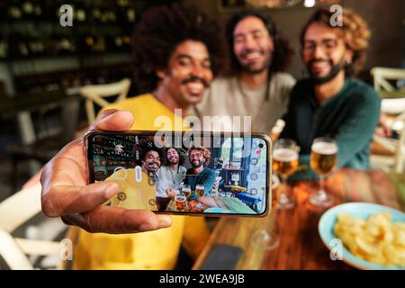 Multiethnic group of three male friends using cellphone to take a selfie in a bar. Stock Photo
