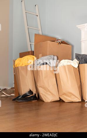 Cardboard boxes with clothes, shoes on the floor things and stuff for moving, Relocation day and moving concept. Vertical photo with copy space. Stock Photo