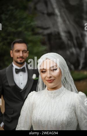 Young happy bride and groom standing in front of a waterfall smiling and posing outdoors Stock Photo