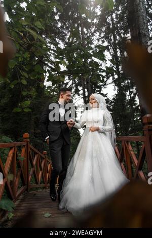 Young bride and groom holding hands, looking each other smiling. Newlywed bride and groom celebrating wedding in forest park Stock Photo