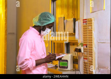 African employee male in sterile uniform writing time card to start working at industrial processing plant Stock Photo