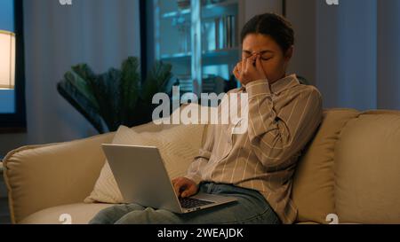 Tired African American woman girl exhausted sleepy female freelancer at night evening home studying online on couch working with laptop typing Stock Photo