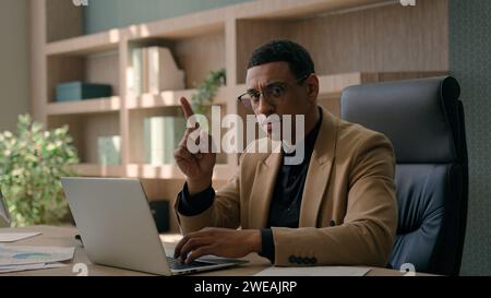 African American ethnic man serious businessman working online on laptop at office dissatisfied male investor business employer waving index finger Stock Photo