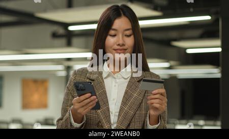 Asian woman business lady Korean girl Chinese client Japanese customer Malaysian businesswoman indoors in office holding mobile phone credit bank Stock Photo
