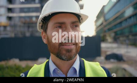 Portrait close up man worker repairman in safety helmet looking around smile male contractor wearing hardhat architect smiling city urban building Stock Photo