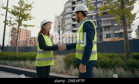 Two people colleagues in safety uniform helmets hardhat engineers managers man and woman female leader male worker builder architects meeting shaking Stock Photo