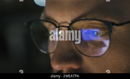 Close up male eyes in glasses eye strain problem medicine night dark man businessman developer computer programmer business man looking at screen blue Stock Photo