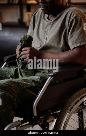 Frustrated senior african american soldier with PTSD in wheelchair holding his headwear Stock Photo