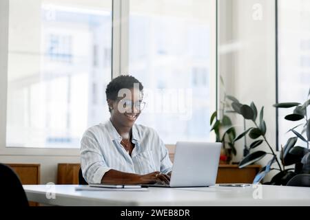 African black businesswoman using laptop at office. Smiling midlle-aged female office employee looking at the laptop screen, Successful woman entrepreneur. Stock Photo