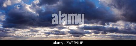 Sun rays shine through dark rainy clouds in the sky. Stock Photo