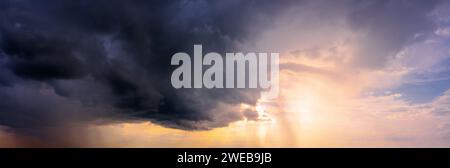 Dramatic sky panorama with bright sun shining through the dark rainy clouds. Natural background. Stock Photo