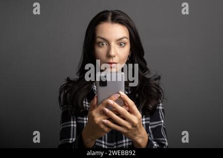 A young woman looking intently and surprised at something on her phone. The female holds a mobile phone in her hands. Stock Photo