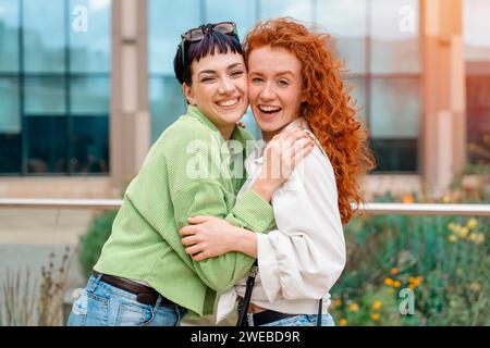 smiling young women girlfriends having a fun time together, talking and using phones at outdoor in urban city. people, communication, friendship and l Stock Photo