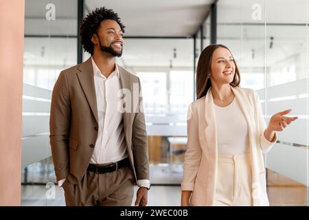In a light-filled office, a man and woman walk together, engaging in a relaxed yet animated conversation that suggests a positive working relationship. Teamwork and a shared vision concept Stock Photo