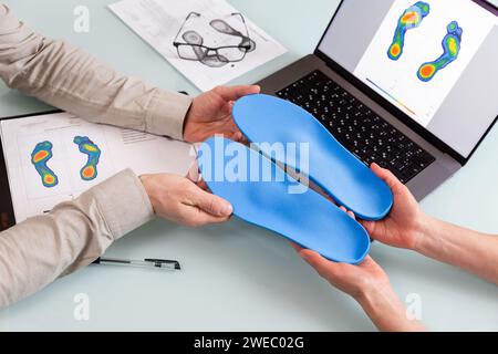 Female doctor orthopedist  presents new custom made insoles to a male patient in a clinic.   Feet recreation and orthotic medicine concept Stock Photo