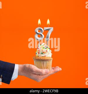 Hand holding birthday cupcake with number 87 candle - background orange Stock Photo