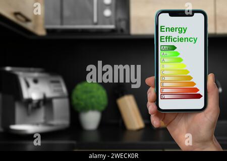 Energy efficiency. Woman using smartphone with colorful rating on display in kitchen, closeup Stock Photo