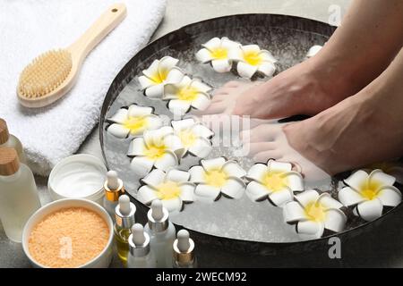 Woman soaking her feet in bowl with water and flowers on floor, closeup. Spa treatment Stock Photo