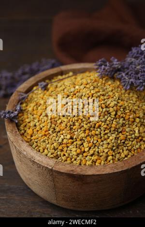 Fresh bee pollen granules in bowl and lavender on wooden table, closeup Stock Photo