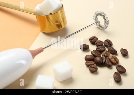 Milk frother wand, coffee beans and sugar cubes on color background, closeup Stock Photo