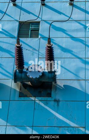 High voltage power lines with ceramic insulators on side of power transfer station building Stock Photo