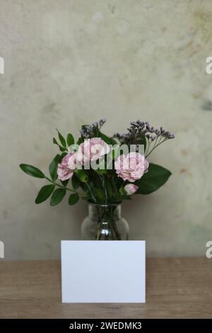 Bouquet of pink carnation flowers in a glass vase with a blank note on the table Stock Photo