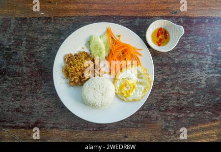 Thai Food Stir-Fried Pork with Garlic and Thai Peppers ontop Fried Crispy Garlic served with Rice ,Fried egg and tomato cucumber carved white plate to Stock Photo