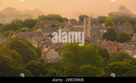 The beautiful stone village of Corfe Castle awakens slowly on an early summer morning with a layer of mist in a warm setting. The village is often ove Stock Photo