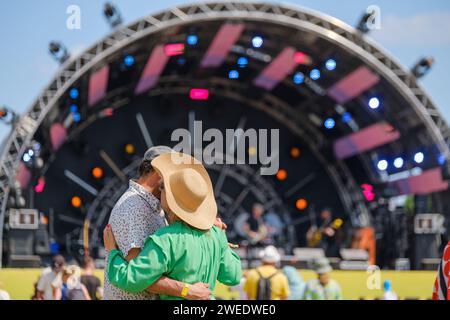 A loving couple hugs and dancing enjoying the ambiance in front of a festival music stage on a sunny day. Stock Photo
