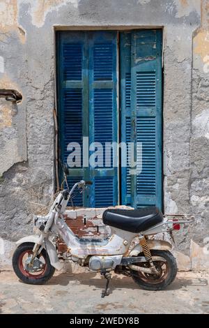 Blue shuttered window and an old motorbike in Greek village Stock Photo