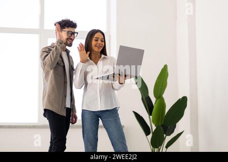 Two focused Indian professional colleagues discussing online application for business, watching Internet startup project, talking on video call on lap Stock Photo