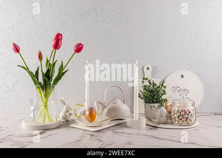 Beautiful festive composition for Easter holiday on marble countertop of light kitchen. candles, a vase of tulips, Easter eggs and bunnies Stock Photo