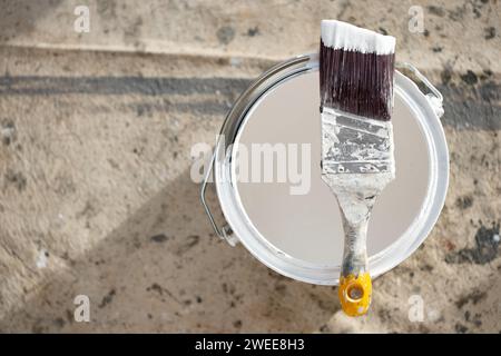 A wooden handled decorators cutting in paint brush with angled bristles  resting on the top of a tin of emulsion paint used for property improvement Stock Photo