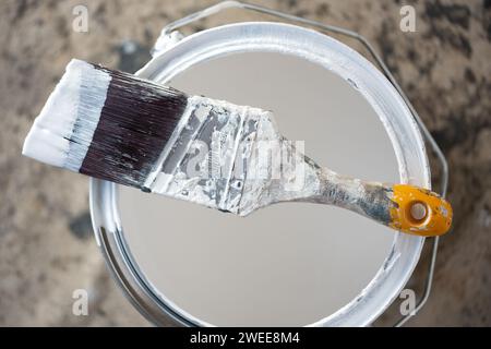 A wooden handled decorators cutting in paint brush with angled bristles  resting on the top of a tin of emulsion paint used for property improvement Stock Photo
