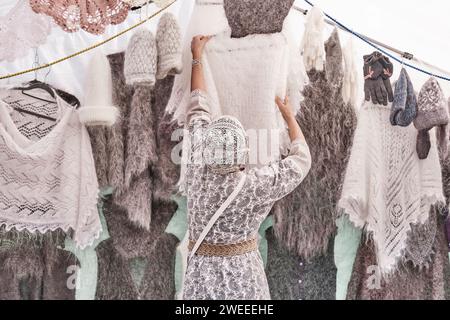 Woman, selling warm knitted items, hanging white fluffy shawl on hanger. Back view. Stock Photo