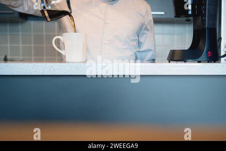 Man in the kitchen pouring a mug of hot filtered coffee from a glass pot in the morning Stock Photo