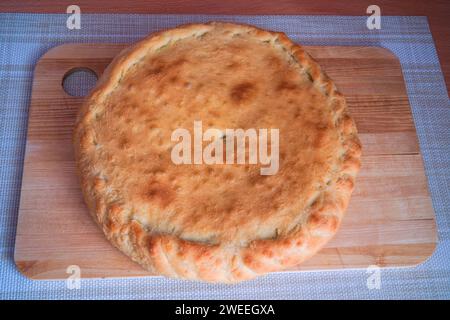 Freshly baked homemade covered pie against the background of a wooden cutting board. Stock Photo