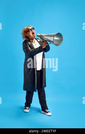 Adult elderly woman dressed in leather trench coat shouting loudly to vintage megaphone to attract people's attention Stock Photo