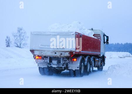 Tipper truck transporting a load of cleared snow away from town to snow dump in winter snowfall. Rear view. Stock Photo