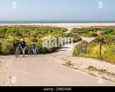 Couple walking with bicycles climbing steep hill of Duinhoevepad in dunes near Renesse on Schouwen-Duiveland, Zeeland, Netherlands Stock Photo