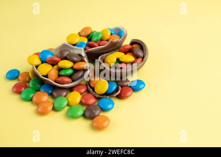 Scattered multi-colored candies in broken Chocolate Easter eggs on yellow background Stock Photo