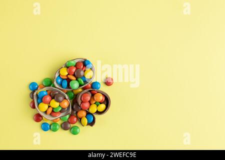 Top view of scattered multi-colored candies in broken Chocolate Easter eggs on yellow background Stock Photo