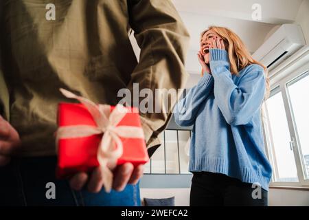Rear view of a man hiding a valentine surprise gift to his girlfriend. Couple celebrating a valentines day holiday. Surprised wife watching a birthday present from her husband. Man giving a giftbox. High quality photo Stock Photo