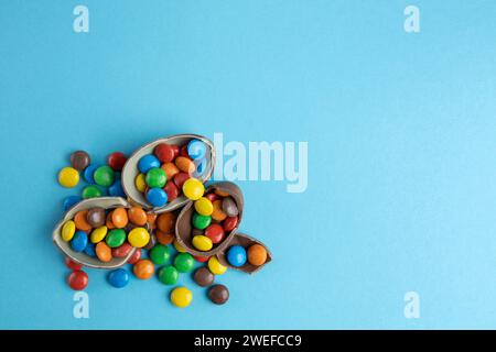 Top view of scattered multi-colored candies in broken Chocolate Easter eggs on blue background Stock Photo