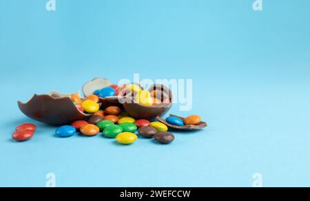 Rainbow candies in broken Chocolate Easter eggs on blue background Stock Photo