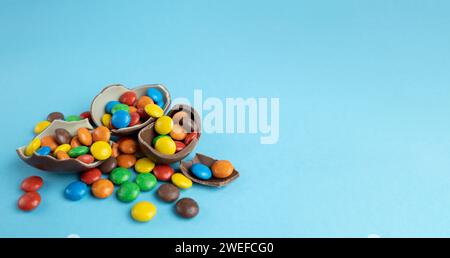 Scattered multi-colored candies in broken Chocolate Easter eggs on blue background Stock Photo