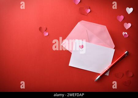 White empty sheet with red pen and open pink envelope on red romantic background with heart cutouts. Top view. Stock Photo