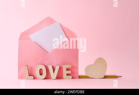 Pink envelope with letters with word love and wooden heart with pencil isolated on pink background. Front view. Stock Photo