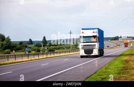 A container truck with a semi-trailer transports cargo from a port to another country along the highway in the summer. Stock Photo